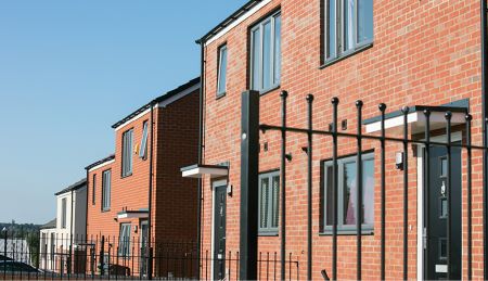 A row of red brick houses with black front doors and black railings.