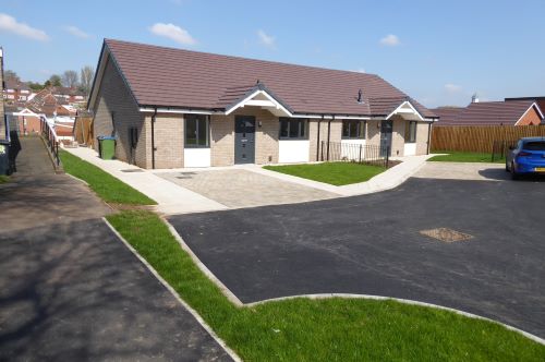 Semi-detached new-build bungalows with stone-effect window frames and charcoal grey front doors.