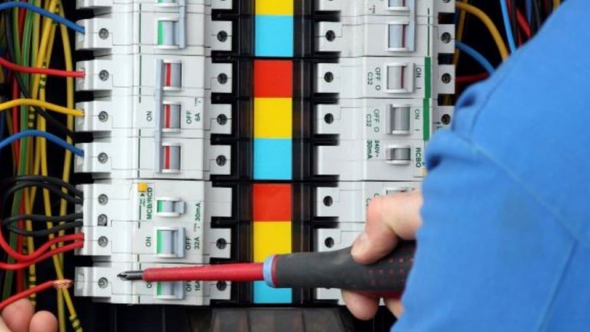 Electrician using a screwdriver on a fuse board.