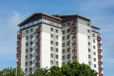 Modern multi-story residential building with multiple balconies and large windows, set against a clear blue sky.