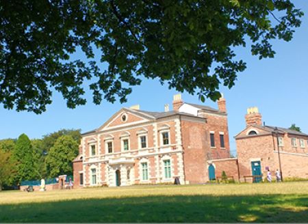 Lightwoods House, a historic brick building with decorative elements, surrounded by greenery and a clear blue sky, featuring two smaller adjacent structures and visitors in the foreground.